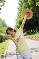 A woman in a yellow shirt and white shorts holding a straw hat.