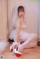 A woman in a wedding dress and high heels sitting on the floor.