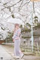 A woman in a kimono holding an umbrella in front of a tree.