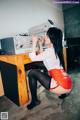 A woman in a red skirt and black stockings sitting at a desk.