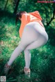 A woman in white leggings and an orange hoodie crouching down in the grass.