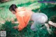 A woman in an orange hoodie crouching down in the grass.