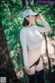 A woman in a white top and black shorts standing in the woods.