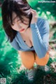 A woman in a blue shirt and orange pants crouching down in the grass.