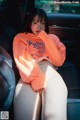 A woman sitting in the back seat of a car wearing an orange sweatshirt.