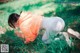 A woman kneeling down in the grass with a flower in her hand.