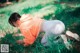 A woman in an orange hoodie and white pants crouching down in the grass.