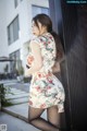 A woman in a floral dress leaning against a wall.