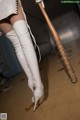 A woman in white thigh high boots holding a baseball bat.