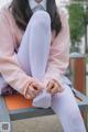 A woman sitting on a bench wearing white tights.