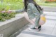 A woman in a green jacket and yellow panties crouching down on a sidewalk.